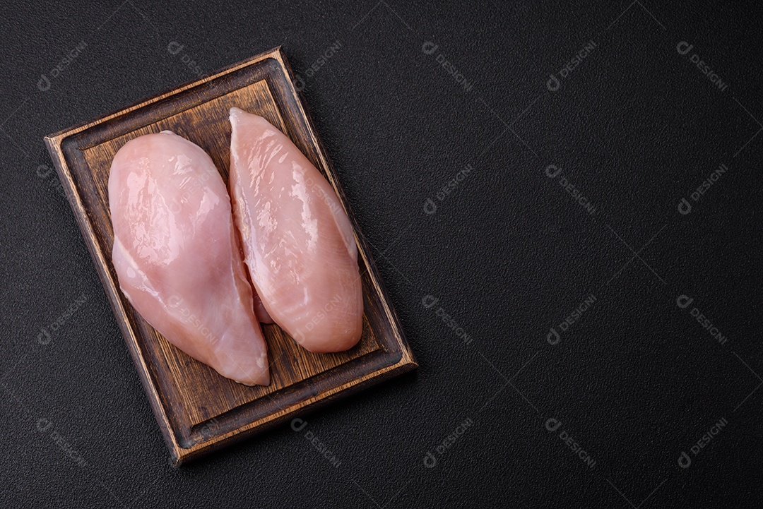 Filé de frango fresco sobre uma mesa de concreto escuro com especiarias e ervas. Preparação para cozinhar pratos de carne