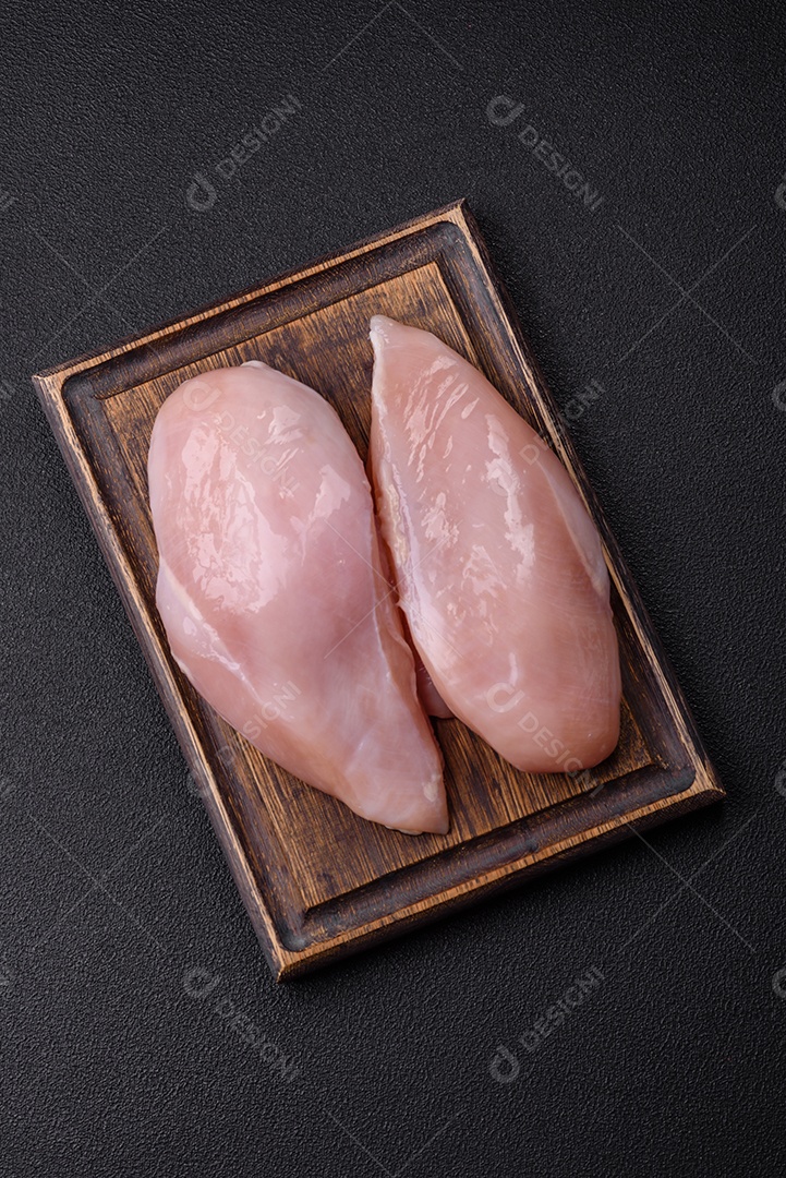 Filé de frango fresco sobre uma mesa de concreto escuro com especiarias e ervas. Preparação para cozinhar pratos de carne