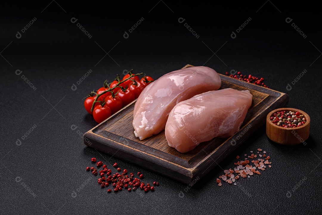 Filé de frango fresco sobre uma mesa de concreto escuro com especiarias e ervas. Preparação para cozinhar pratos de carne