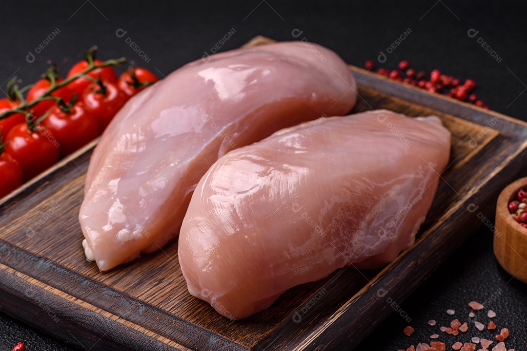 Filé de frango fresco sobre uma mesa de concreto escuro com especiarias e ervas. Preparação para cozinhar pratos de carne