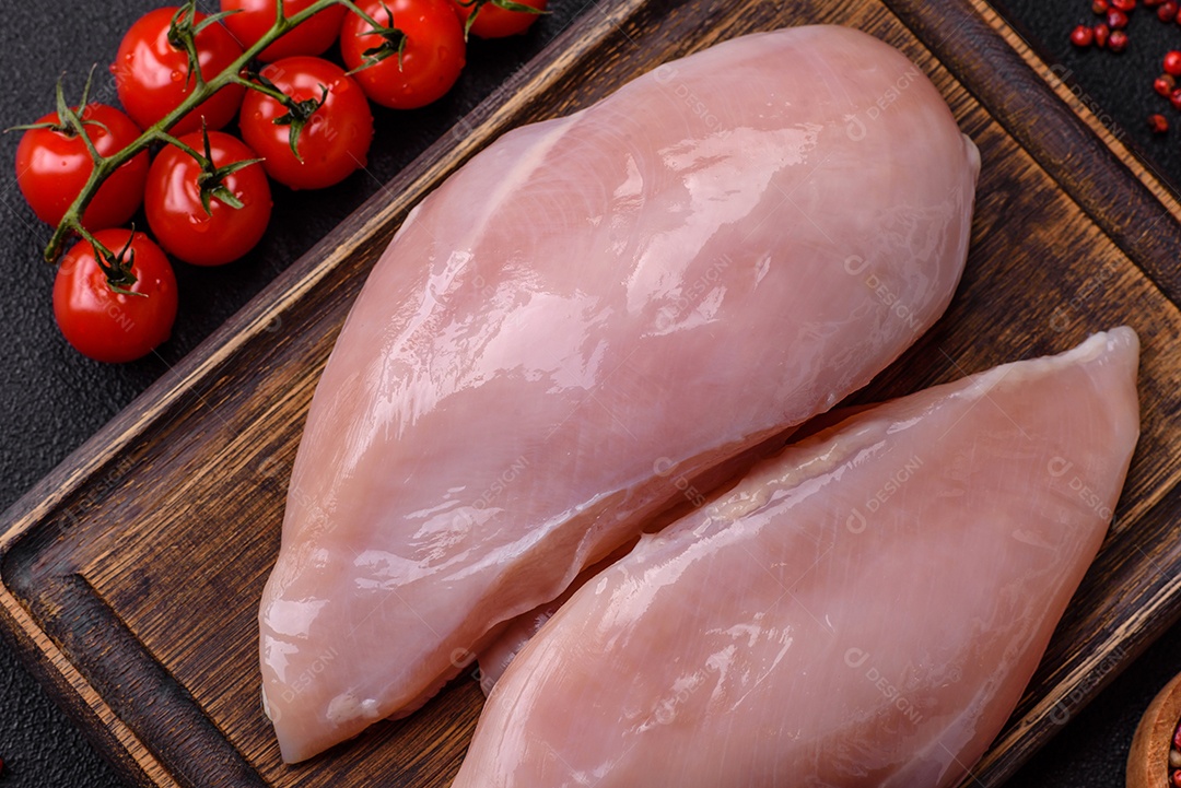 Filé de frango fresco sobre uma mesa de concreto escuro com especiarias e ervas. Preparação para cozinhar pratos de carne