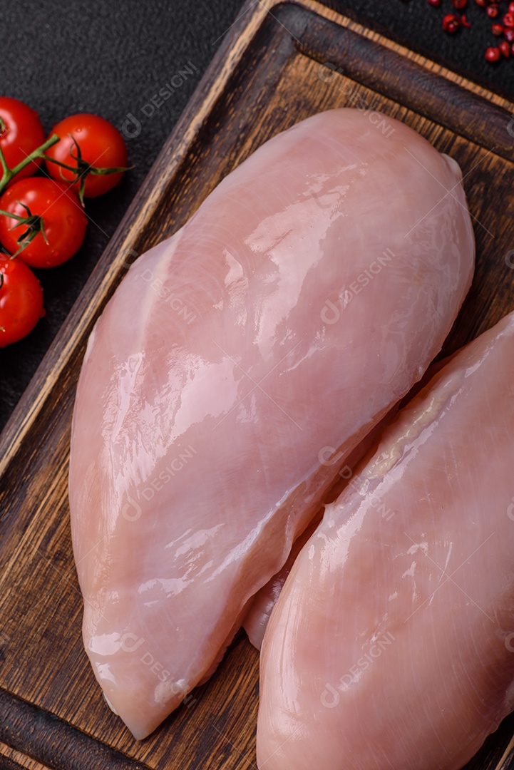 Filé de frango fresco sobre uma mesa de concreto escuro com especiarias e ervas. Preparação para cozinhar pratos de carne