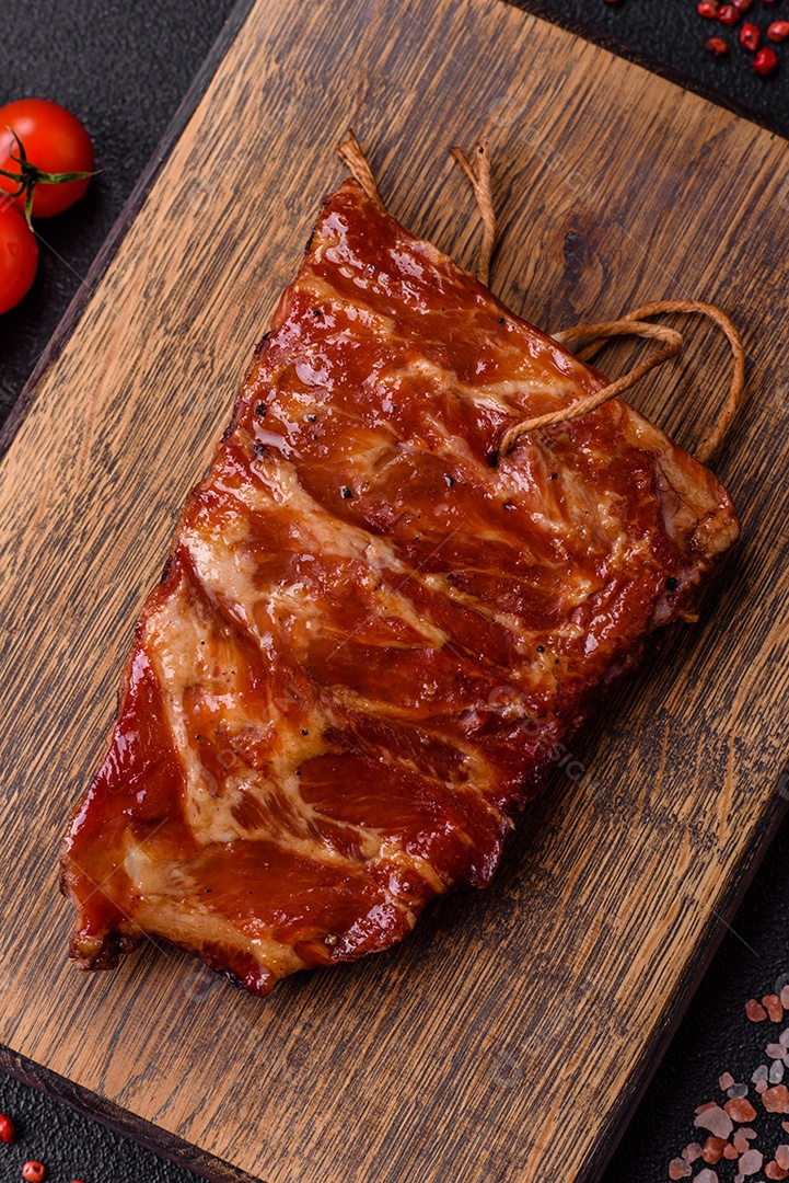 Deliciosas costelas grelhadas assadas na grelha com sal, especiarias e ervas sobre um fundo escuro de concreto