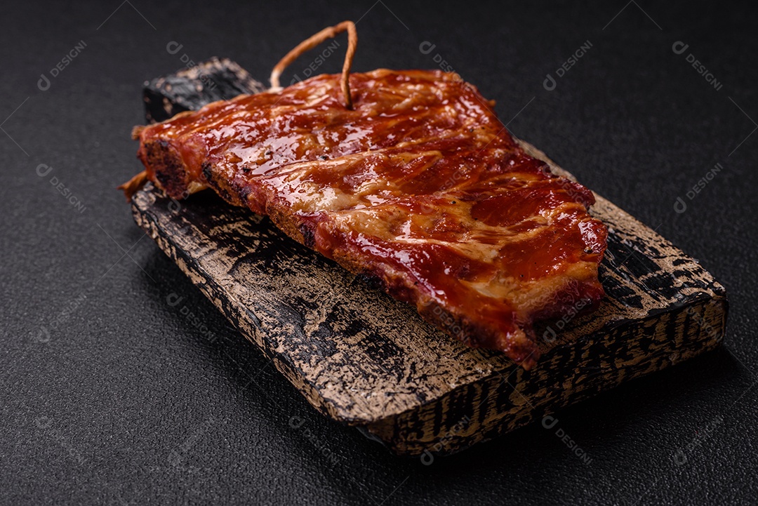 Deliciosas costelas grelhadas assadas na grelha com sal, especiarias e ervas sobre um fundo escuro de concreto