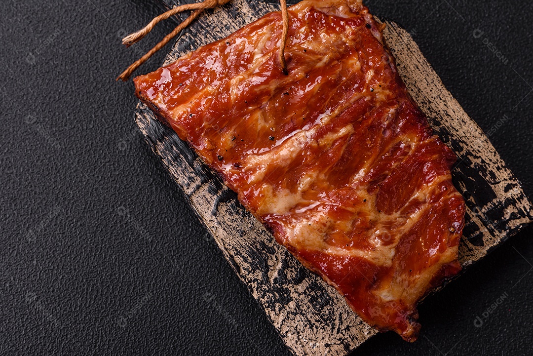 Deliciosas costelas grelhadas assadas na grelha com sal, especiarias e ervas sobre um fundo escuro de concreto