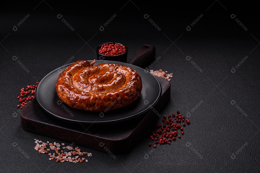 Deliciosa salsicha caseira em forma de espiral assada na grelha com sal, especiarias e ervas sobre um fundo escuro de concreto