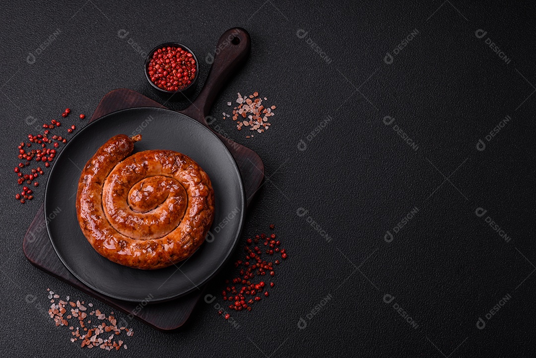 Deliciosa salsicha caseira em forma de espiral assada na grelha com sal, especiarias e ervas sobre um fundo escuro de concreto