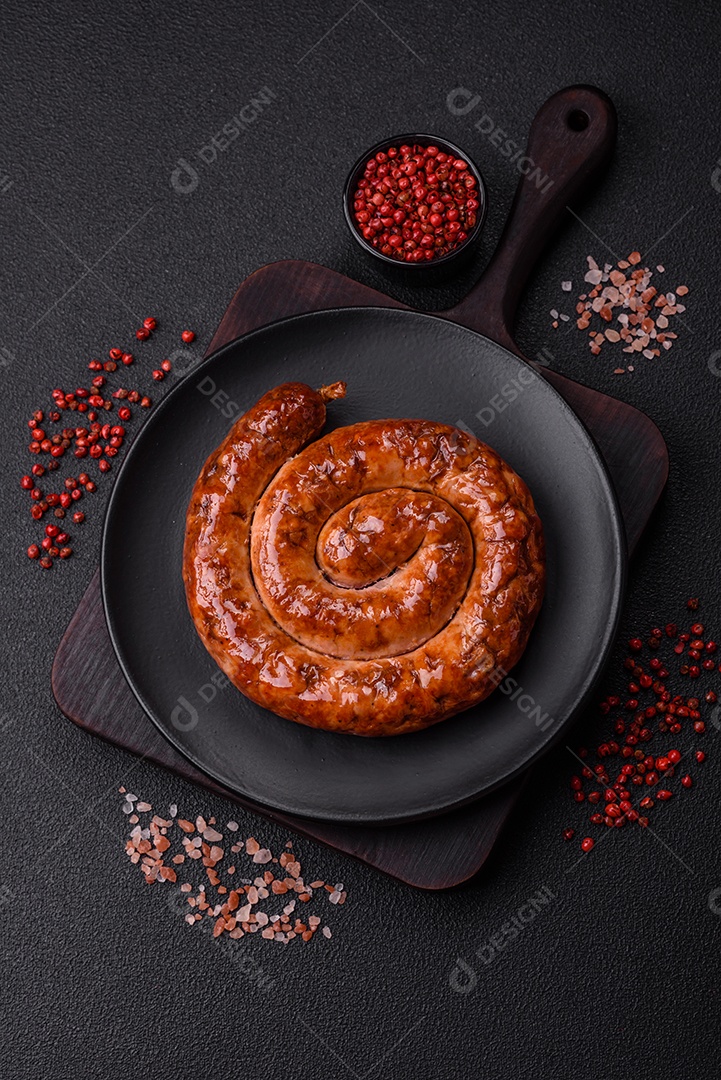 Deliciosa salsicha caseira em forma de espiral assada na grelha com sal, especiarias e ervas sobre um fundo escuro de concreto
