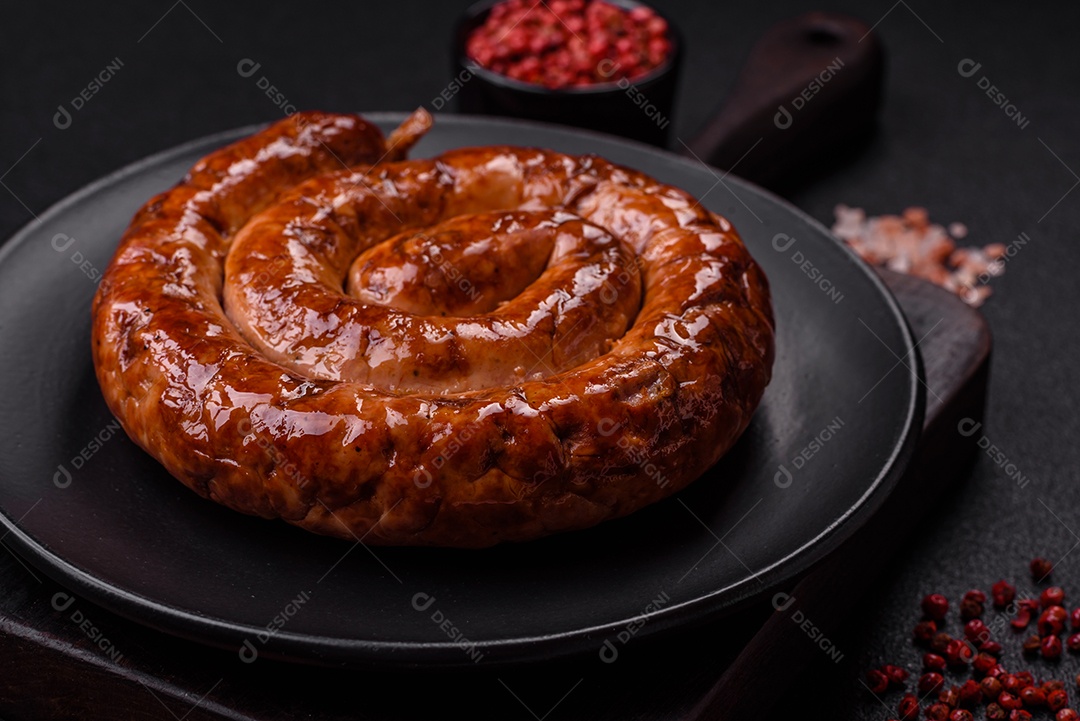 Deliciosa salsicha caseira em forma de espiral assada na grelha com sal, especiarias e ervas sobre um fundo escuro de concreto