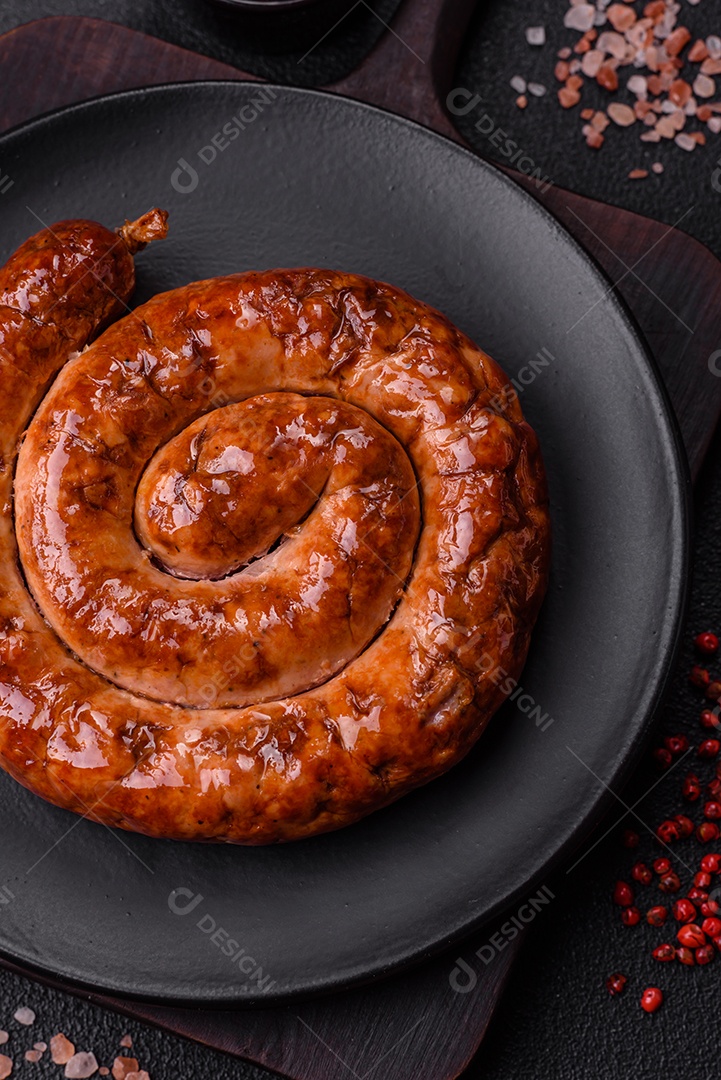 Deliciosa salsicha caseira em forma de espiral assada na grelha com sal, especiarias e ervas sobre um fundo escuro de concreto
