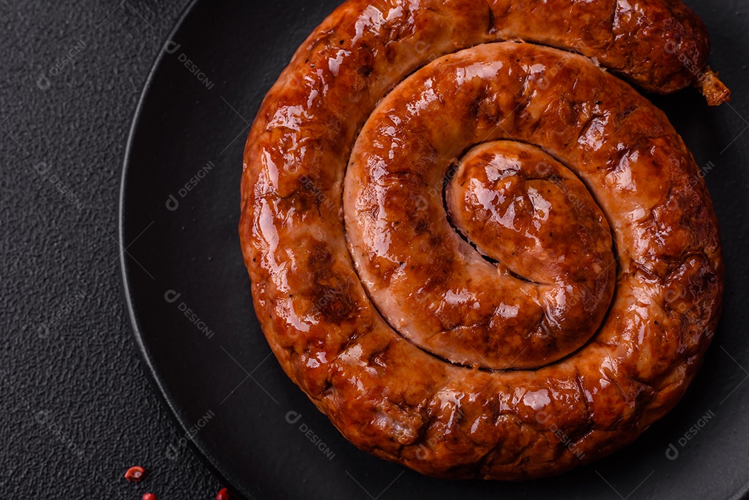 Deliciosa salsicha caseira em forma de espiral assada na grelha com sal, especiarias e ervas sobre um fundo escuro de concreto