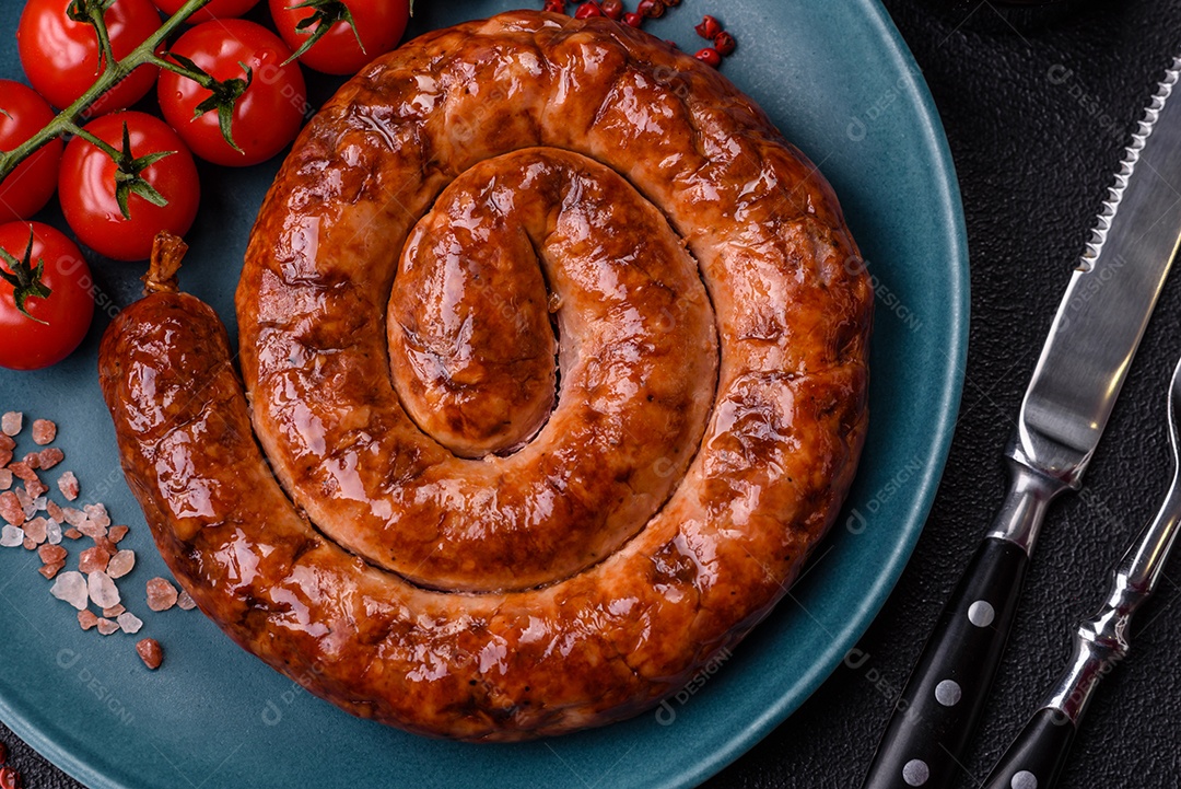 Deliciosa salsicha caseira em forma de espiral assada na grelha com sal, especiarias e ervas sobre um fundo escuro de concreto