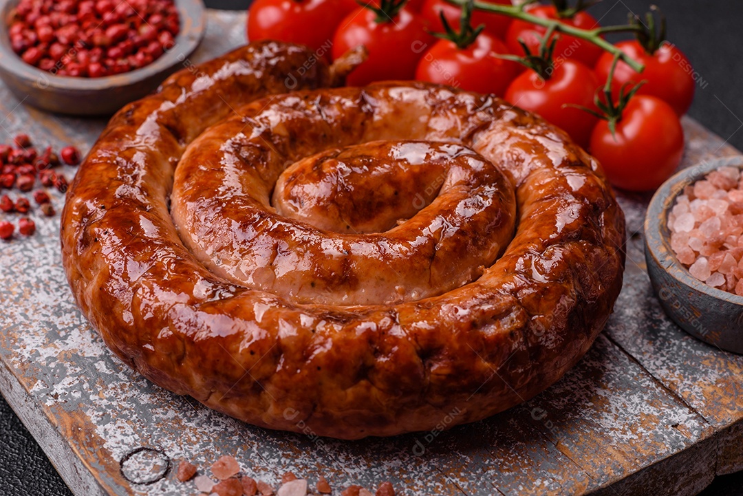 Deliciosa salsicha caseira em forma de espiral assada na grelha com sal, especiarias e ervas sobre um fundo escuro de concreto