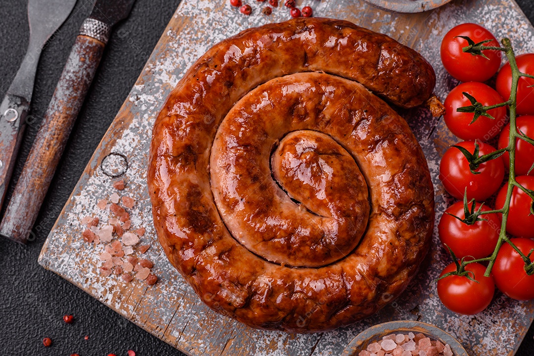 Deliciosa salsicha caseira em forma de espiral assada na grelha com sal, especiarias e ervas sobre um fundo escuro de concreto