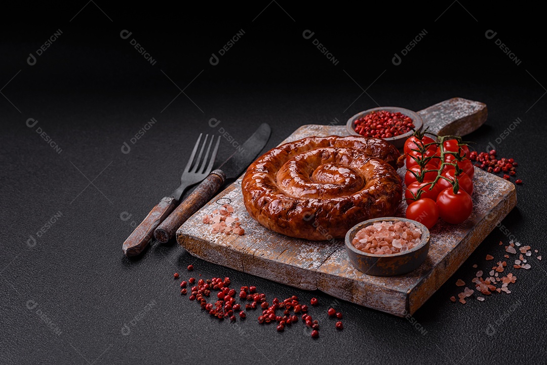 Deliciosa salsicha caseira em forma de espiral assada na grelha com sal, especiarias e ervas sobre um fundo escuro de concreto