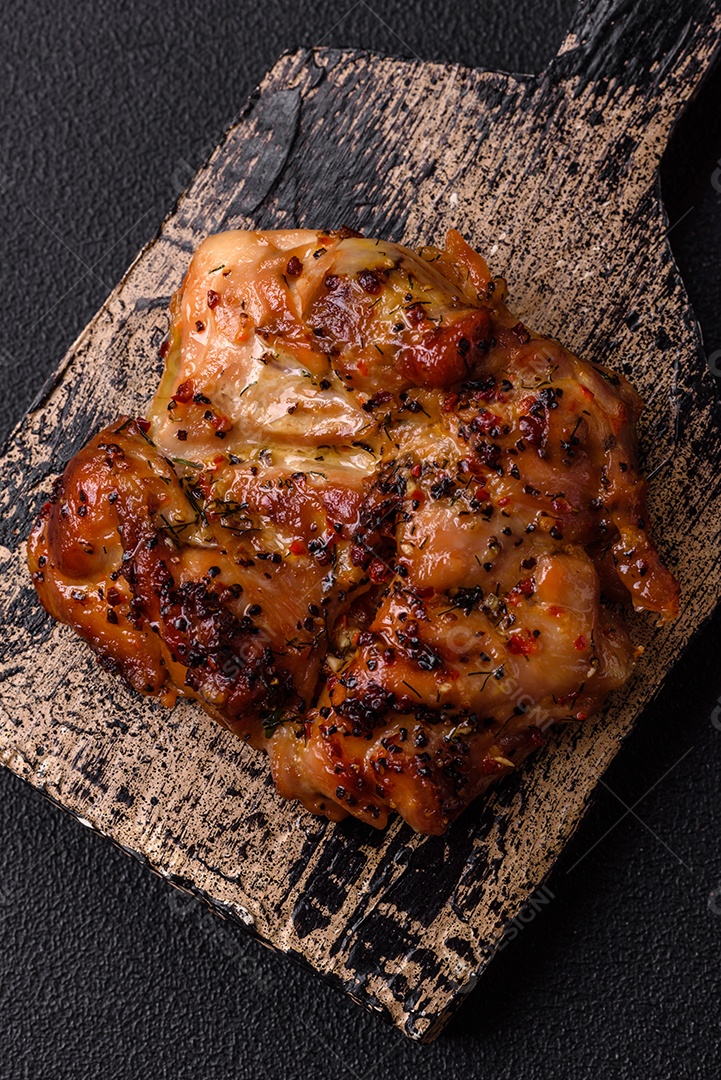 Delicioso bife de frango suculento com sal, especiarias e ervas sobre um fundo escuro de concreto