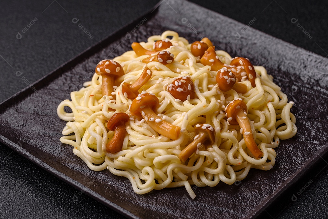 Delicioso prato de cozinha asiática com macarrão de arroz, pimentão, cogumelos e especiarias sobre fundo escuro de concreto