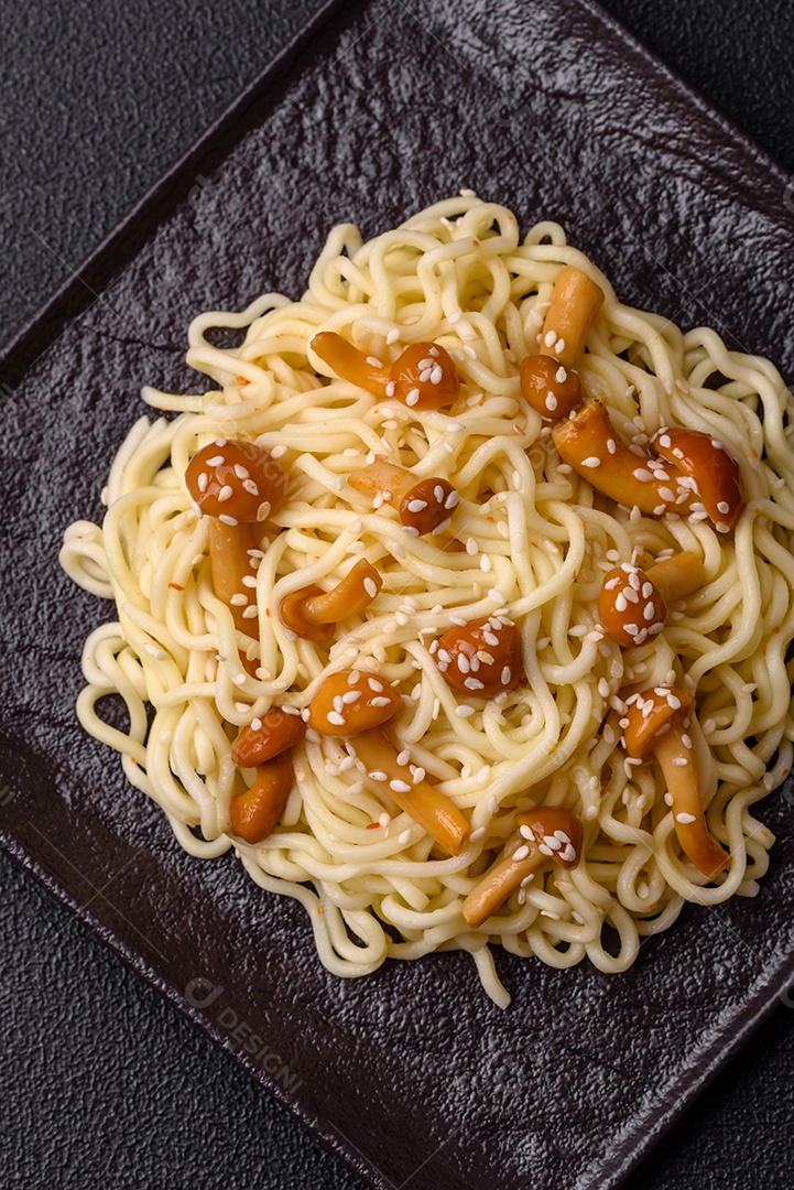 Delicioso prato de cozinha asiática com macarrão de arroz, pimentão, cogumelos e especiarias sobre fundo escuro de concreto