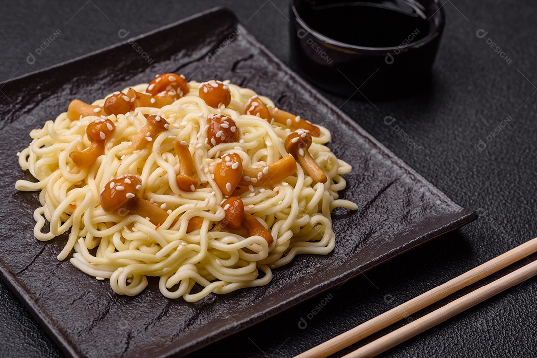 Delicioso prato de cozinha asiática com macarrão de arroz, pimentão, cogumelos e especiarias sobre fundo escuro de concreto