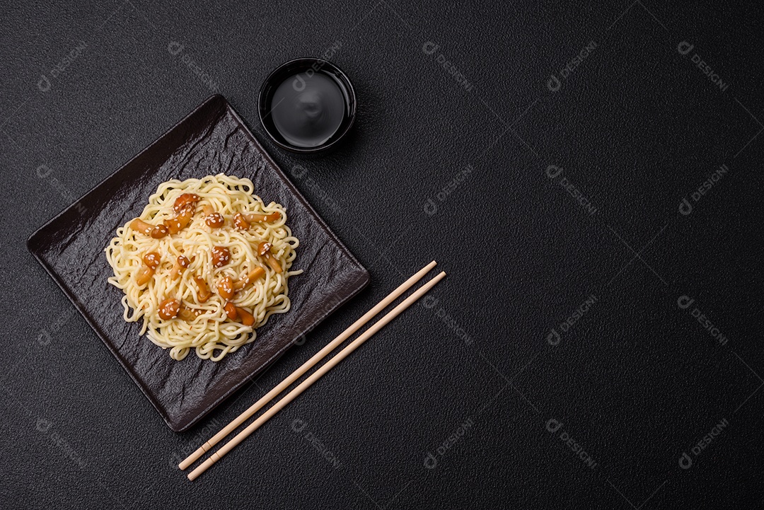 Delicioso prato de cozinha asiática com macarrão de arroz, pimentão, cogumelos e especiarias sobre fundo escuro de concreto