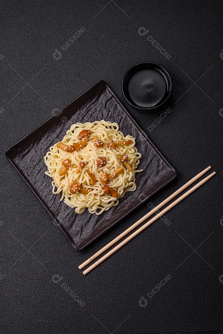 Delicioso prato de cozinha asiática com macarrão de arroz, pimentão, cogumelos e especiarias sobre fundo escuro de concreto