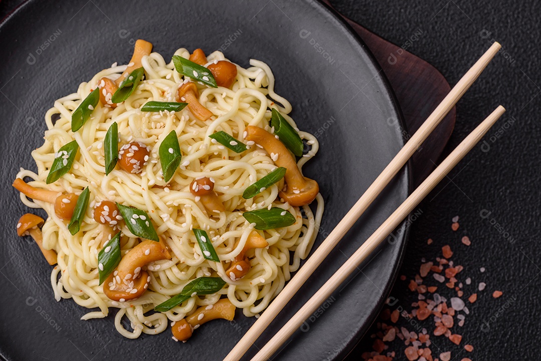 Delicioso prato de cozinha asiática com macarrão de arroz, pimentão, cogumelos e especiarias sobre fundo escuro de concreto