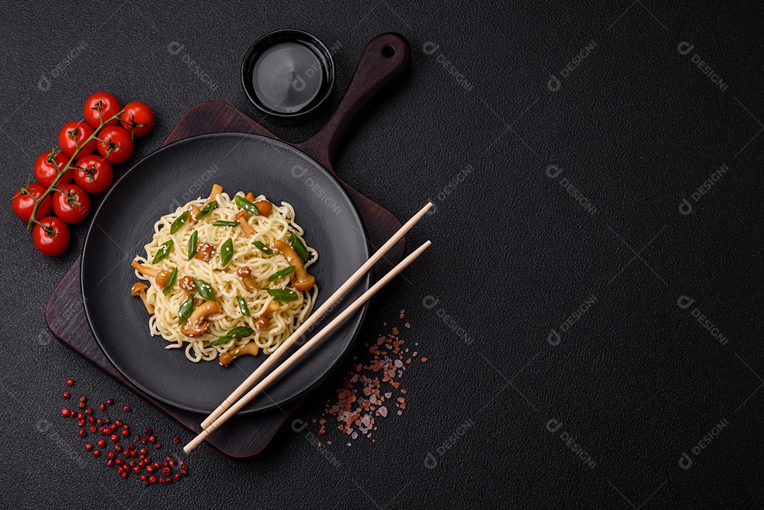 Delicioso prato de cozinha asiática com macarrão de arroz, pimentão, cogumelos e especiarias sobre fundo escuro de concreto