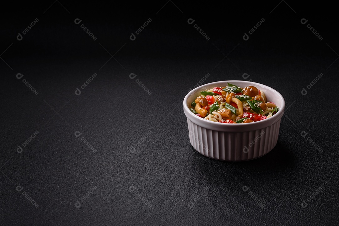 Delicioso prato de cozinha asiática com macarrão de arroz, pimentão, cogumelos e especiarias sobre fundo escuro de concreto