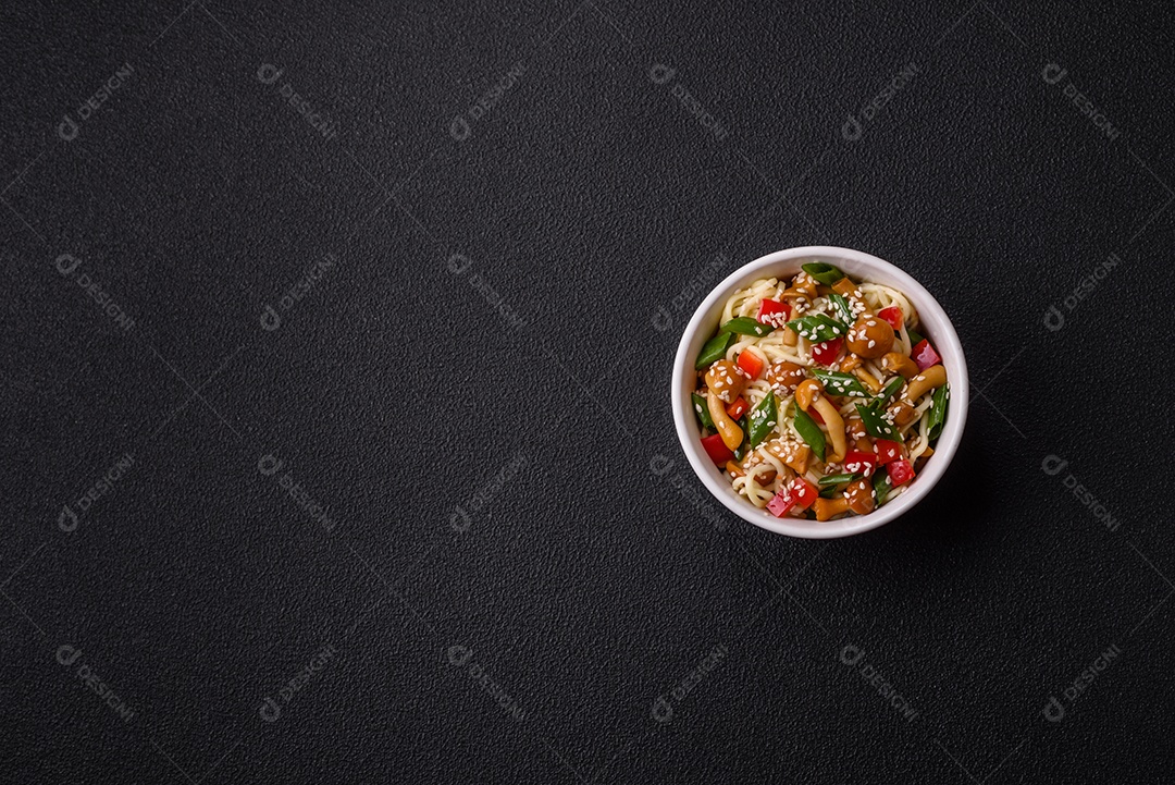 Delicioso prato de cozinha asiática com macarrão de arroz, pimentão, cogumelos e especiarias sobre fundo escuro de concreto