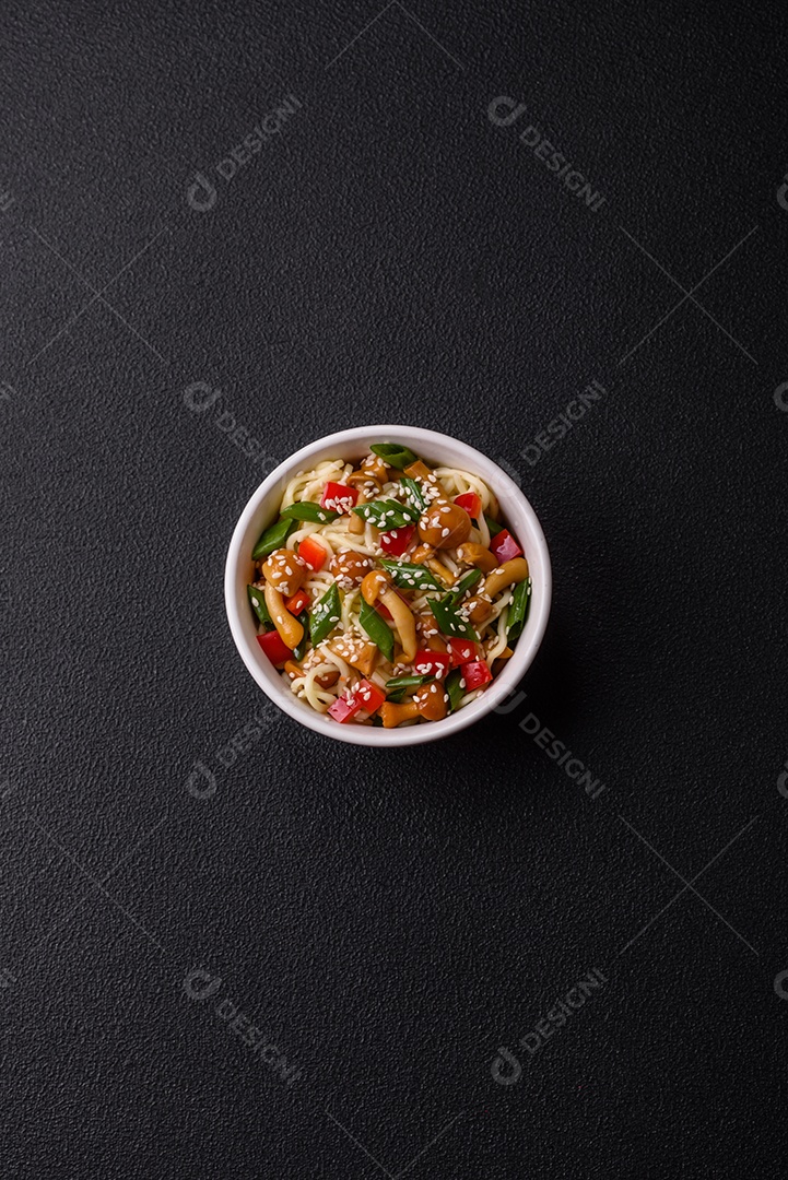 Delicioso prato de cozinha asiática com macarrão de arroz, pimentão, cogumelos e especiarias sobre fundo escuro de concreto
