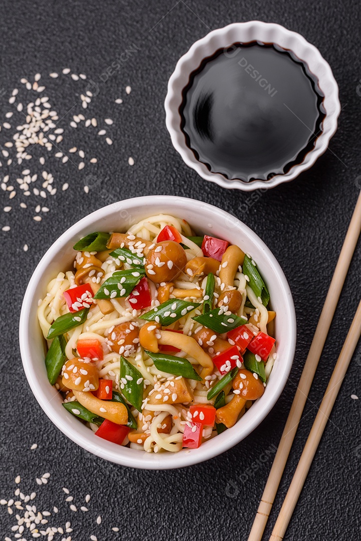 Delicioso prato de cozinha asiática com macarrão de arroz, pimentão, cogumelos e especiarias sobre fundo escuro de concreto
