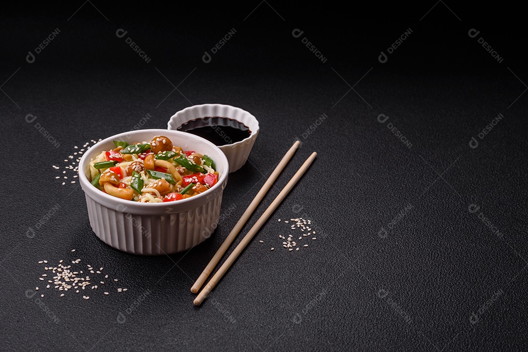 Delicioso prato de cozinha asiática com macarrão de arroz, pimentão, cogumelos e especiarias sobre fundo escuro de concreto