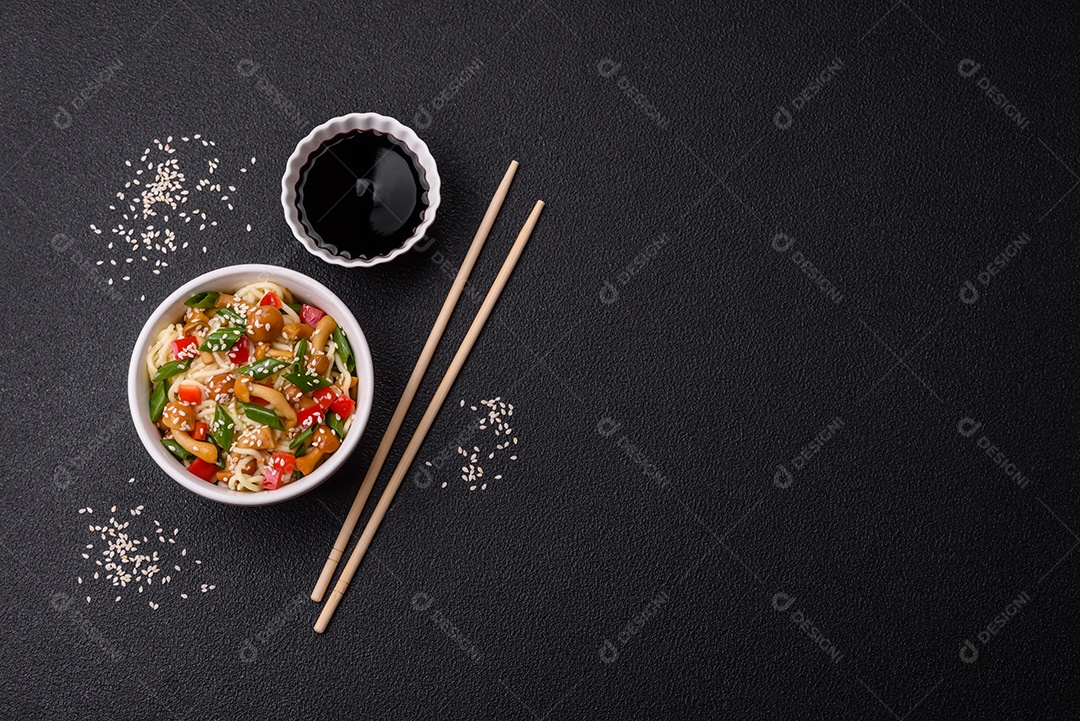 Delicioso prato de cozinha asiática com macarrão de arroz, pimentão, cogumelos e especiarias sobre fundo escuro de concreto