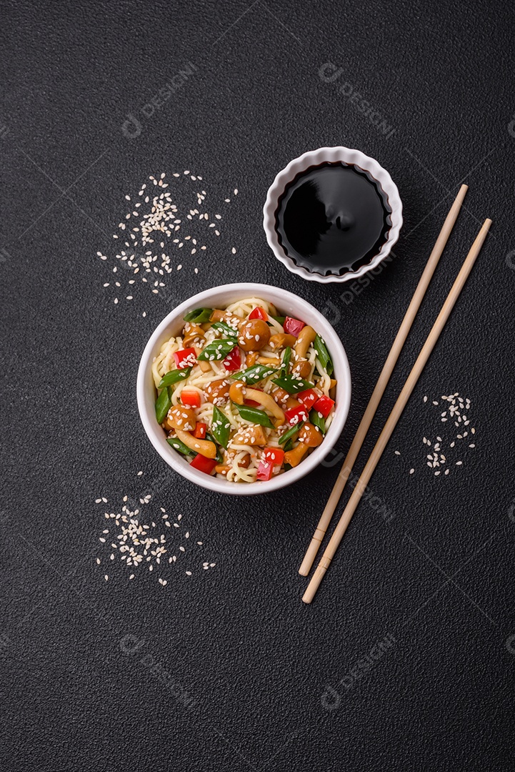Delicioso prato de cozinha asiática com macarrão de arroz, pimentão, cogumelos e especiarias sobre fundo escuro de concreto