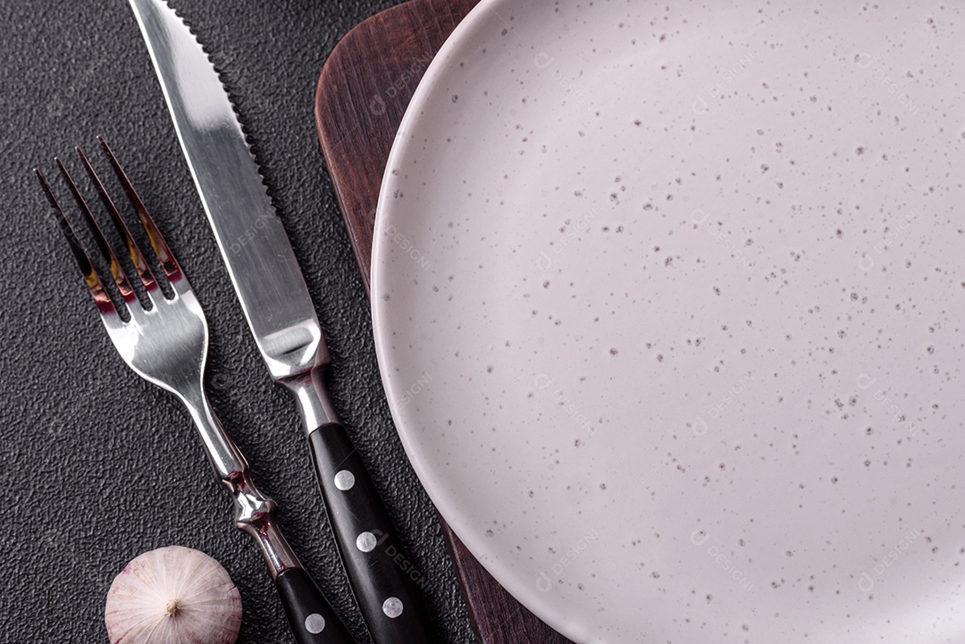 Placa redonda de cerâmica vazia em fundo de concreto texturizado escuro. Talheres, preparação para o jantar