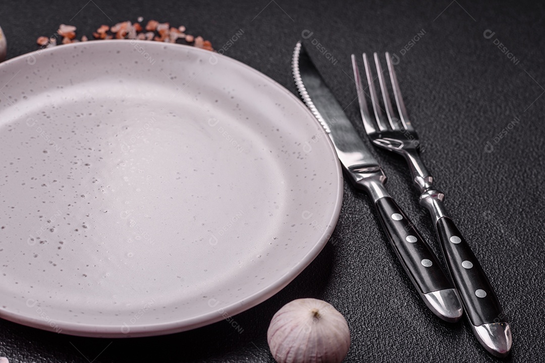 Placa redonda de cerâmica vazia em fundo de concreto texturizado escuro. Talheres, preparação para o jantar
