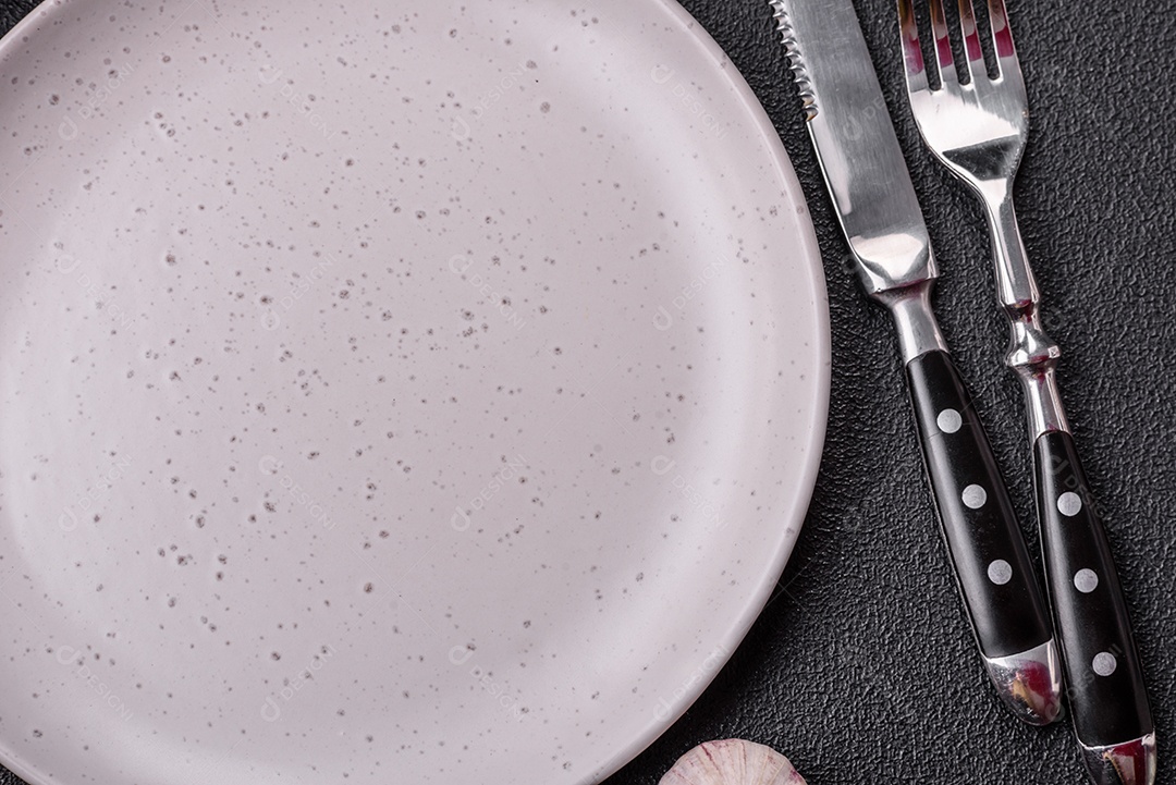 Placa redonda de cerâmica vazia em fundo de concreto texturizado escuro. Talheres, preparação para o jantar