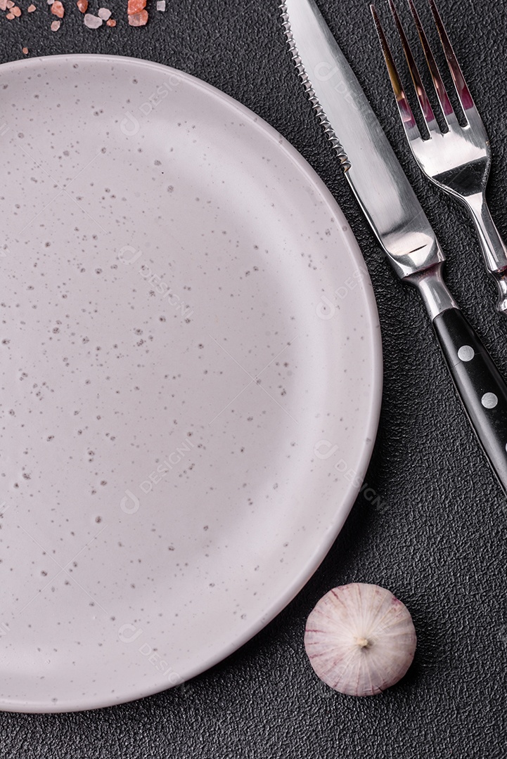 Placa redonda de cerâmica vazia em fundo de concreto texturizado escuro. Talheres, preparação para o jantar