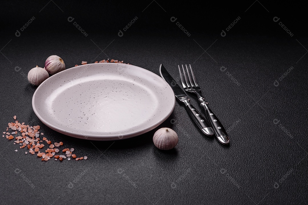 Placa redonda de cerâmica vazia em fundo de concreto texturizado escuro. Talheres, preparação para o jantar