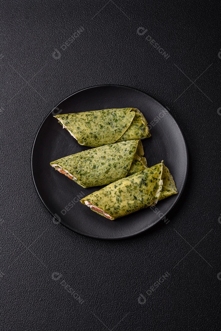 Deliciosas panquecas caseiras com espinafre, salmão, queijo Filadélfia com sal, especiarias e ervas sobre fundo escuro de concreto