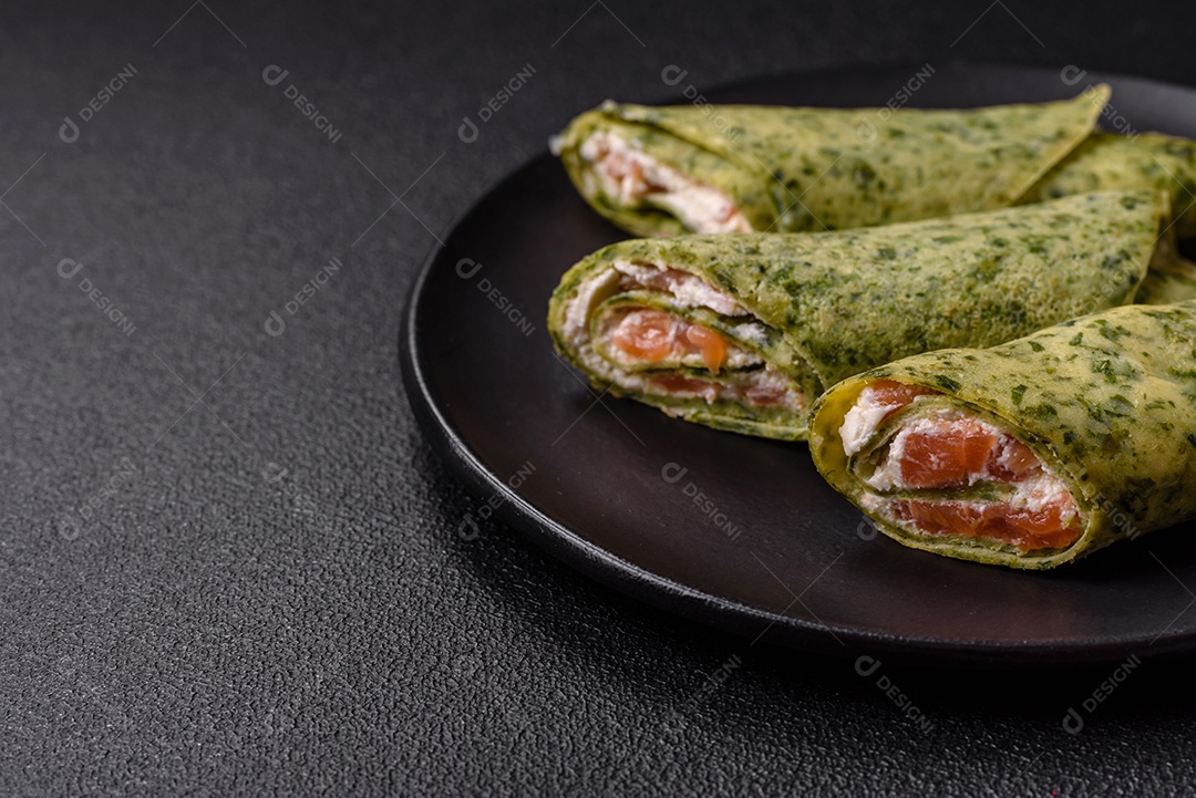 Deliciosas panquecas caseiras com espinafre, salmão, queijo Filadélfia com sal, especiarias e ervas sobre fundo escuro de concreto