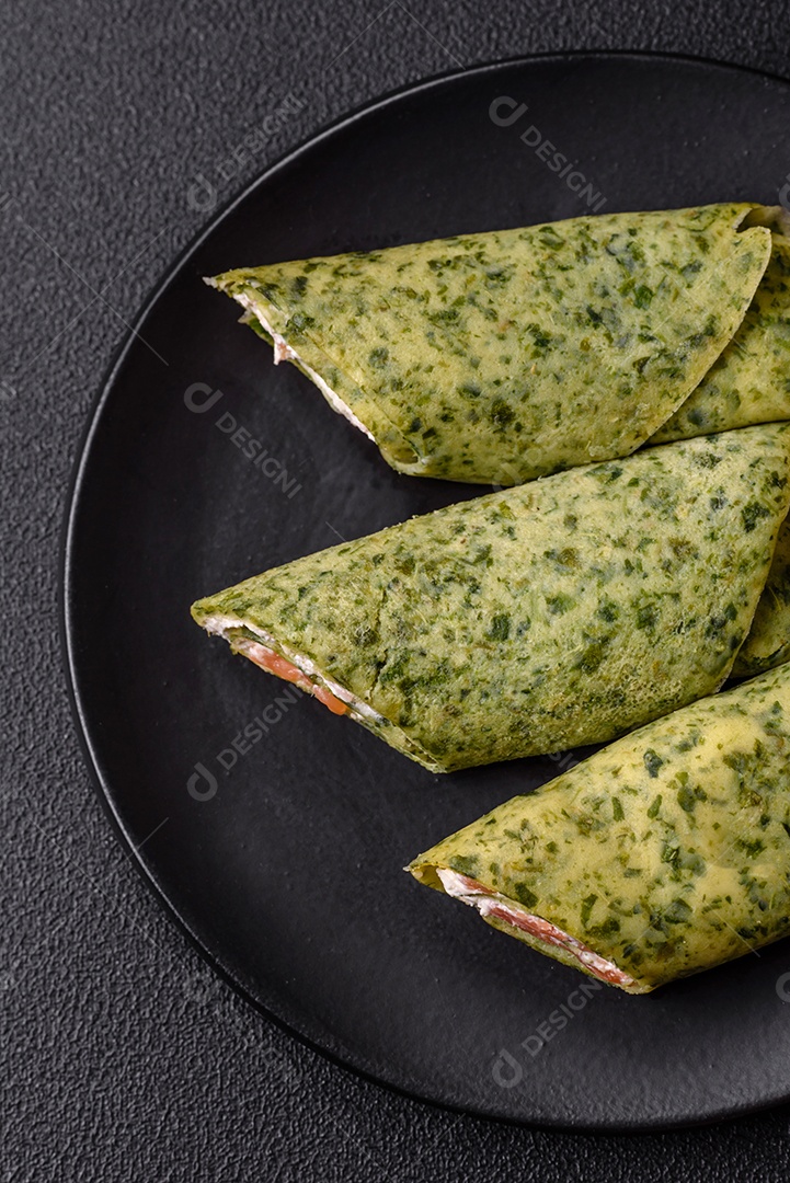 Deliciosas panquecas caseiras com espinafre, salmão, queijo Filadélfia com sal, especiarias e ervas sobre fundo escuro de concreto