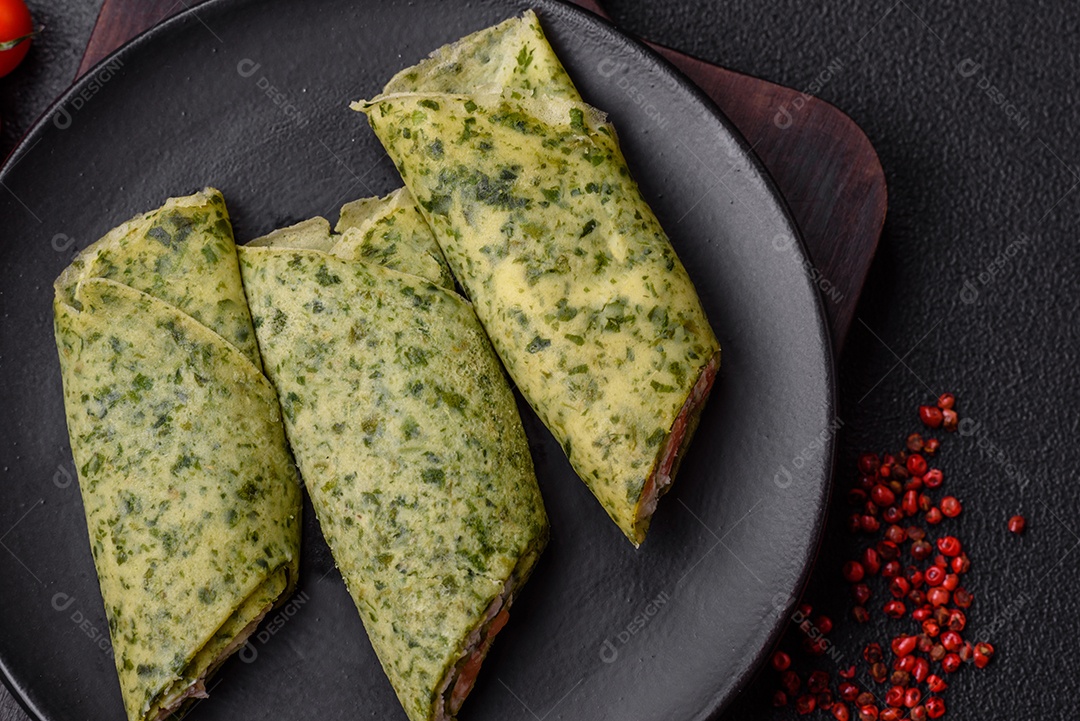 Deliciosas panquecas caseiras com espinafre, salmão, queijo Filadélfia com sal, especiarias e ervas sobre fundo escuro de concreto