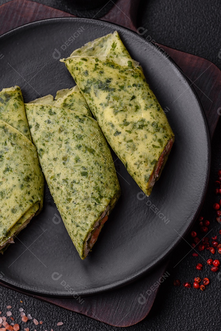 Deliciosas panquecas caseiras com espinafre, salmão, queijo Filadélfia com sal, especiarias e ervas sobre fundo escuro de concreto
