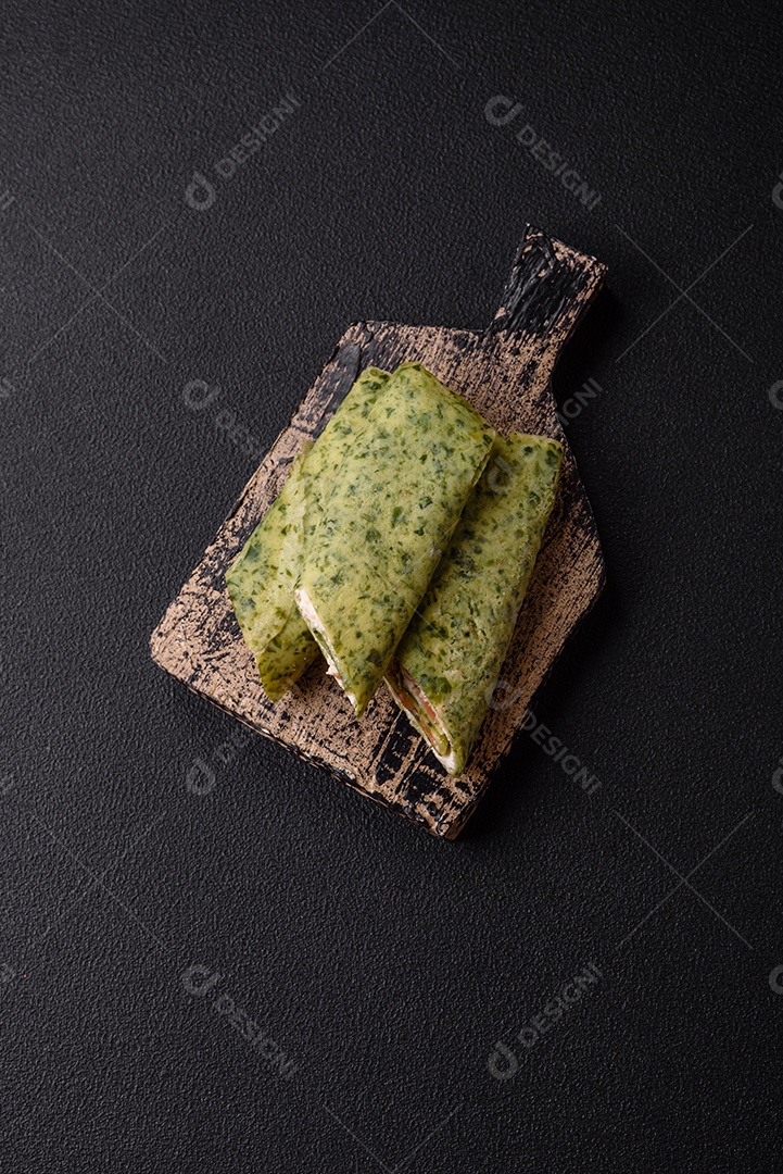 Deliciosas panquecas caseiras com espinafre, salmão, queijo Filadélfia com sal, especiarias e ervas sobre fundo escuro de concreto