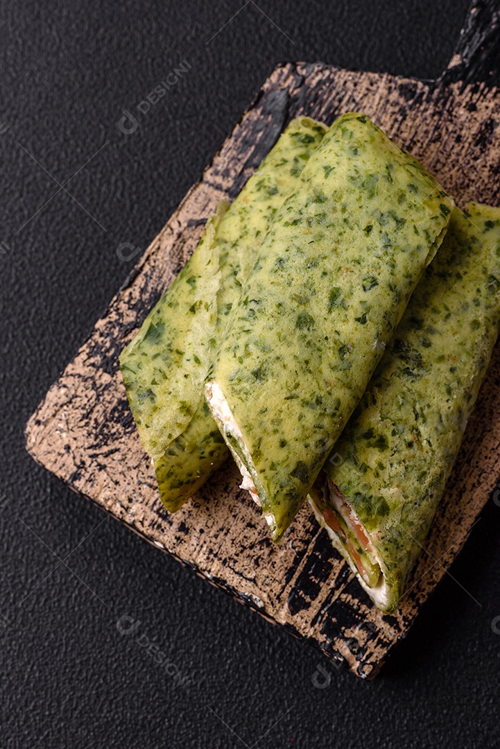 Deliciosas panquecas caseiras com espinafre, salmão, queijo Filadélfia com sal, especiarias e ervas sobre fundo escuro de concreto