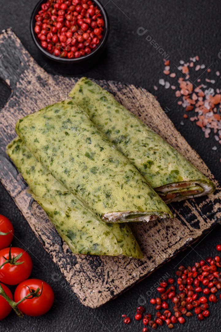 Deliciosas panquecas caseiras com espinafre, salmão, queijo Filadélfia com sal, especiarias e ervas sobre fundo escuro de concreto