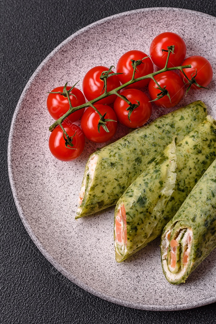 Deliciosas panquecas caseiras com espinafre, salmão, queijo Filadélfia com sal, especiarias e ervas sobre fundo escuro de concreto