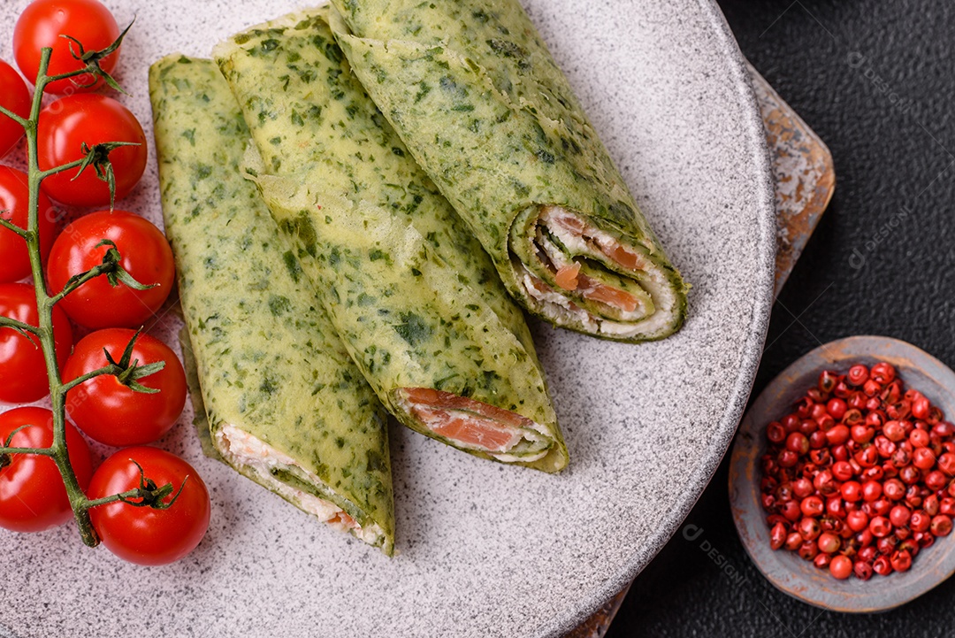 Deliciosas panquecas caseiras com espinafre, salmão, queijo Filadélfia com sal, especiarias e ervas sobre fundo escuro de concreto