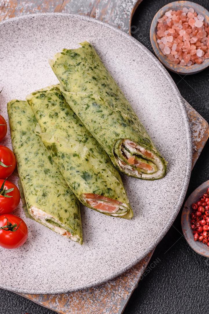 Deliciosas panquecas caseiras com espinafre, salmão, queijo Filadélfia com sal, especiarias e ervas sobre fundo escuro de concreto